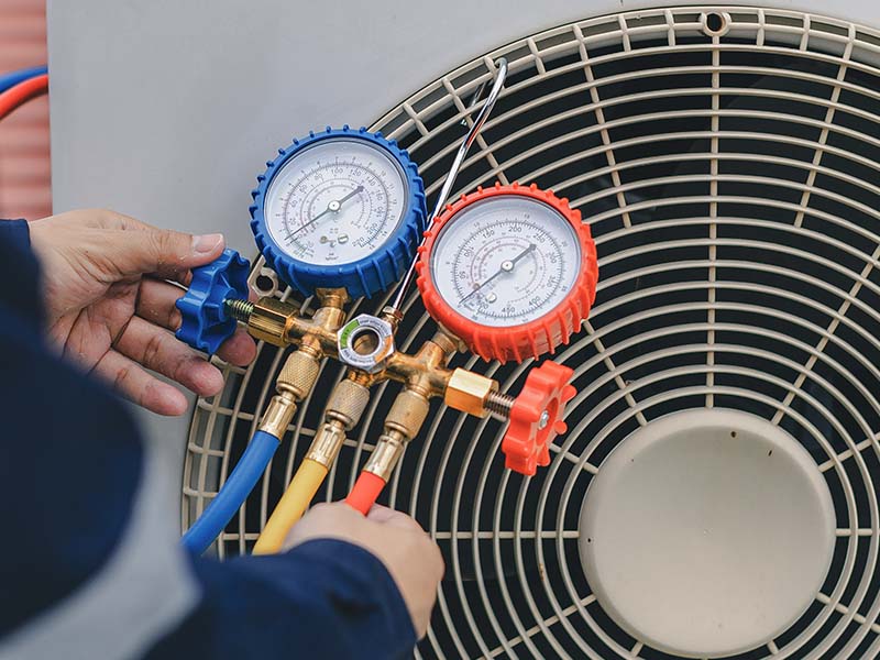 Closeup of HVAC technician holding a manifold gauge in from of an outdoor AC unit.