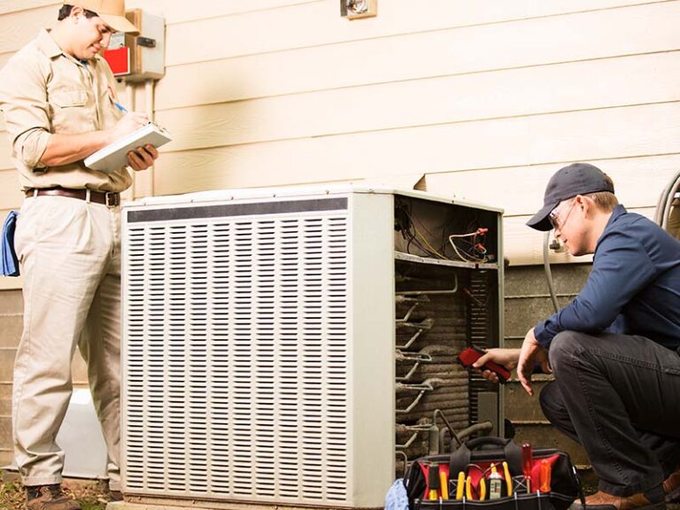 Two HVAC technicians completing maintenance checks on outdoor HVAC condenser.