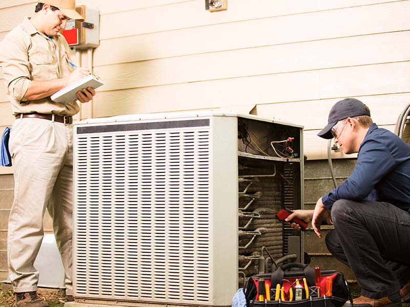 Two HVAC technicians completing maintenance checks on outdoor HVAC condenser.