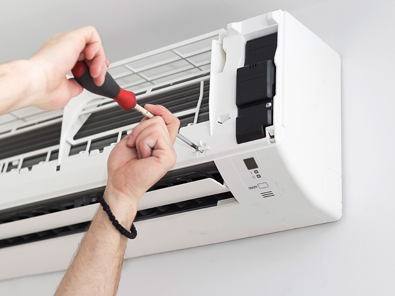 Closeup of technician securing a ductless indoor unit to a wall using a screwdriver.