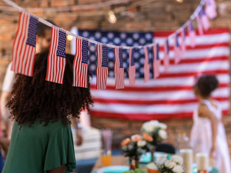 4th of July decorative banner with an American falg in the background.