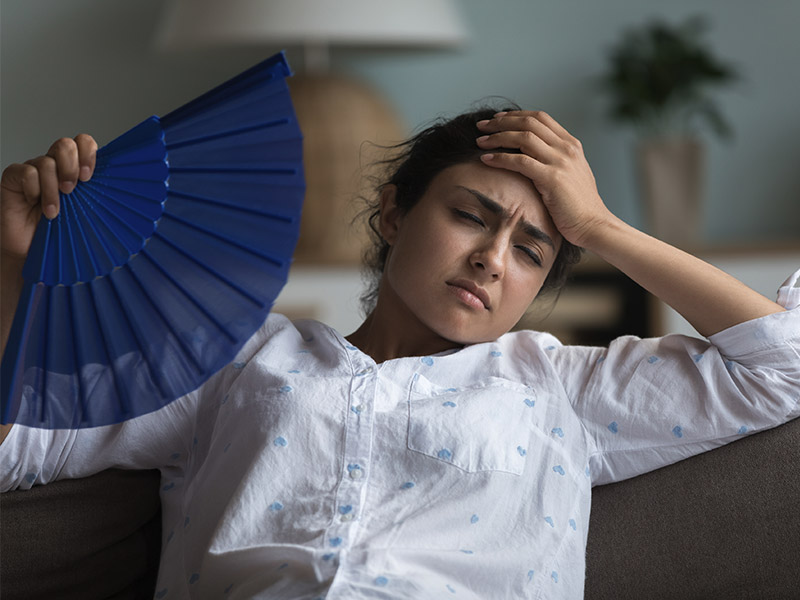 Woman using a paper fan to cool herself down in a hot living room.