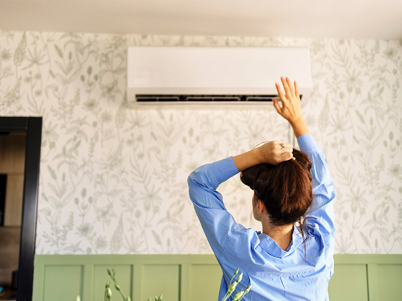 Woman holding her hand up to a mini split HVAC wall mounted unit.