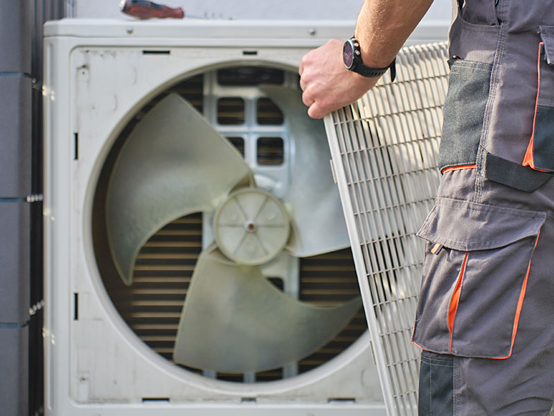HVAC technician removing cover from an outdoor heat pump unit to perform maintenance.
